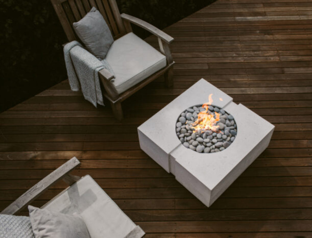 Fire pit table with flames on a wooden deck with chairs and cushions.