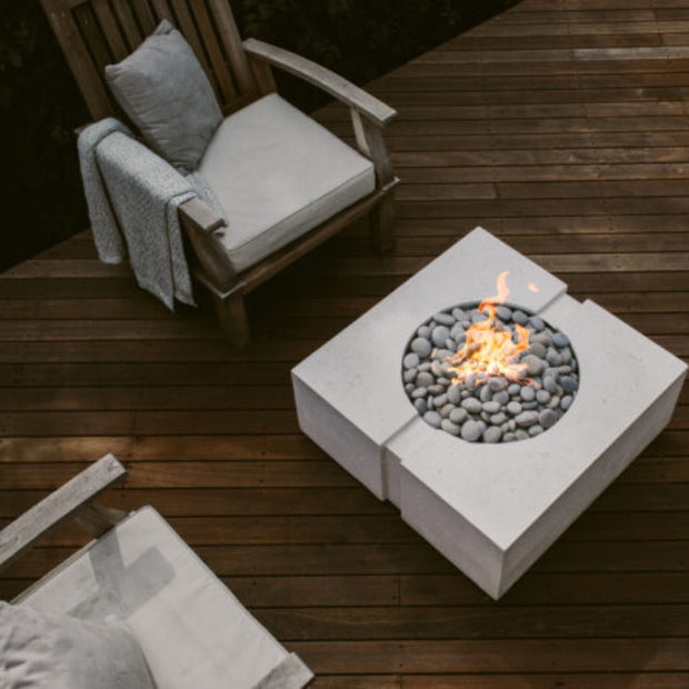 Fire pit table with flames on a wooden deck with chairs and cushions.