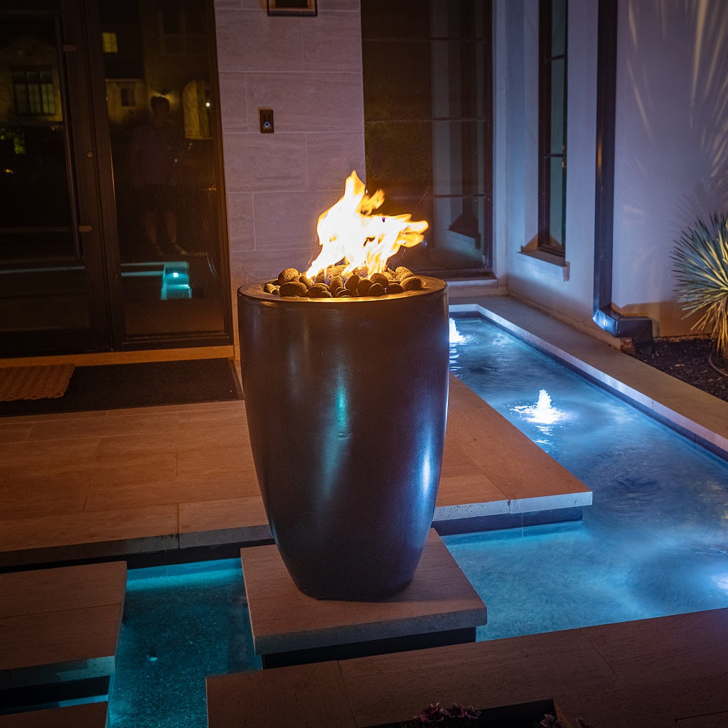 Fire pit by a pool at night with flames and water reflections.