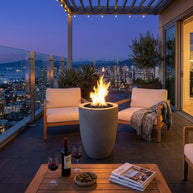 Outdoor patio with fire pit, chairs, and cityscape view at night.
