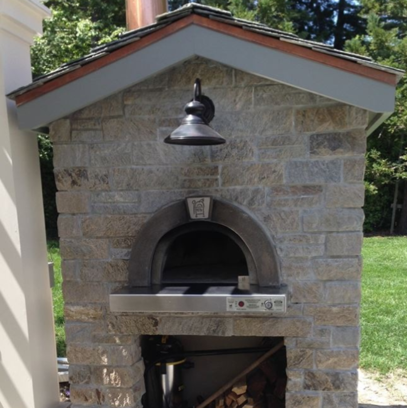 Outdoor stone Pizza oven with wood storage area in a garden setting