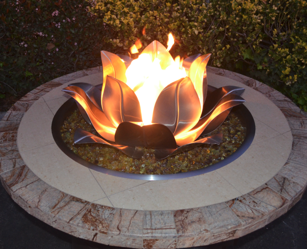 Fire pit with a decorative flame Lotus Flower design on a stone base outdoors.