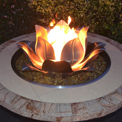Fire pit with a decorative flame Lotus Flower design on a stone base outdoors.