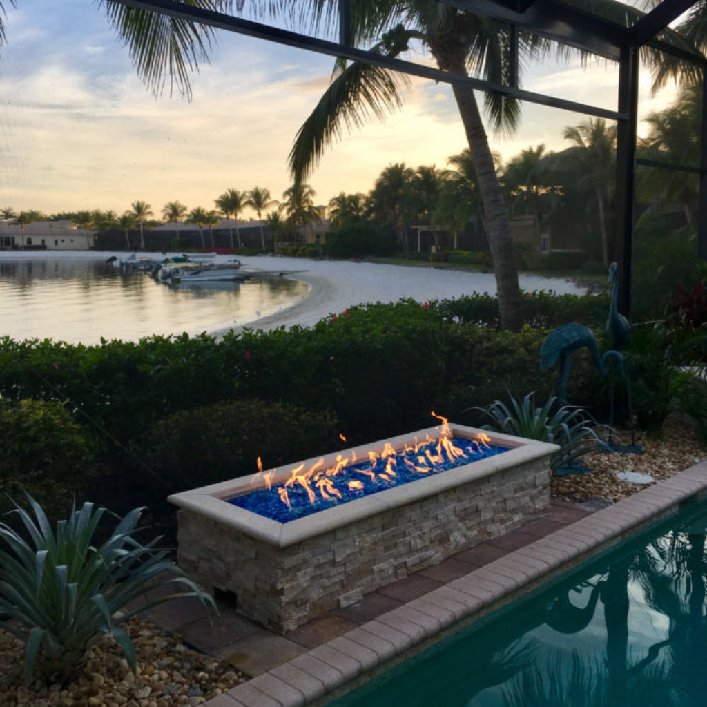 Fire pit by a pool with palm trees and water in the background