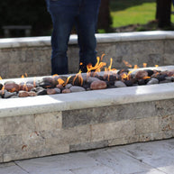 Fire pit with flames and stones, person standing nearby