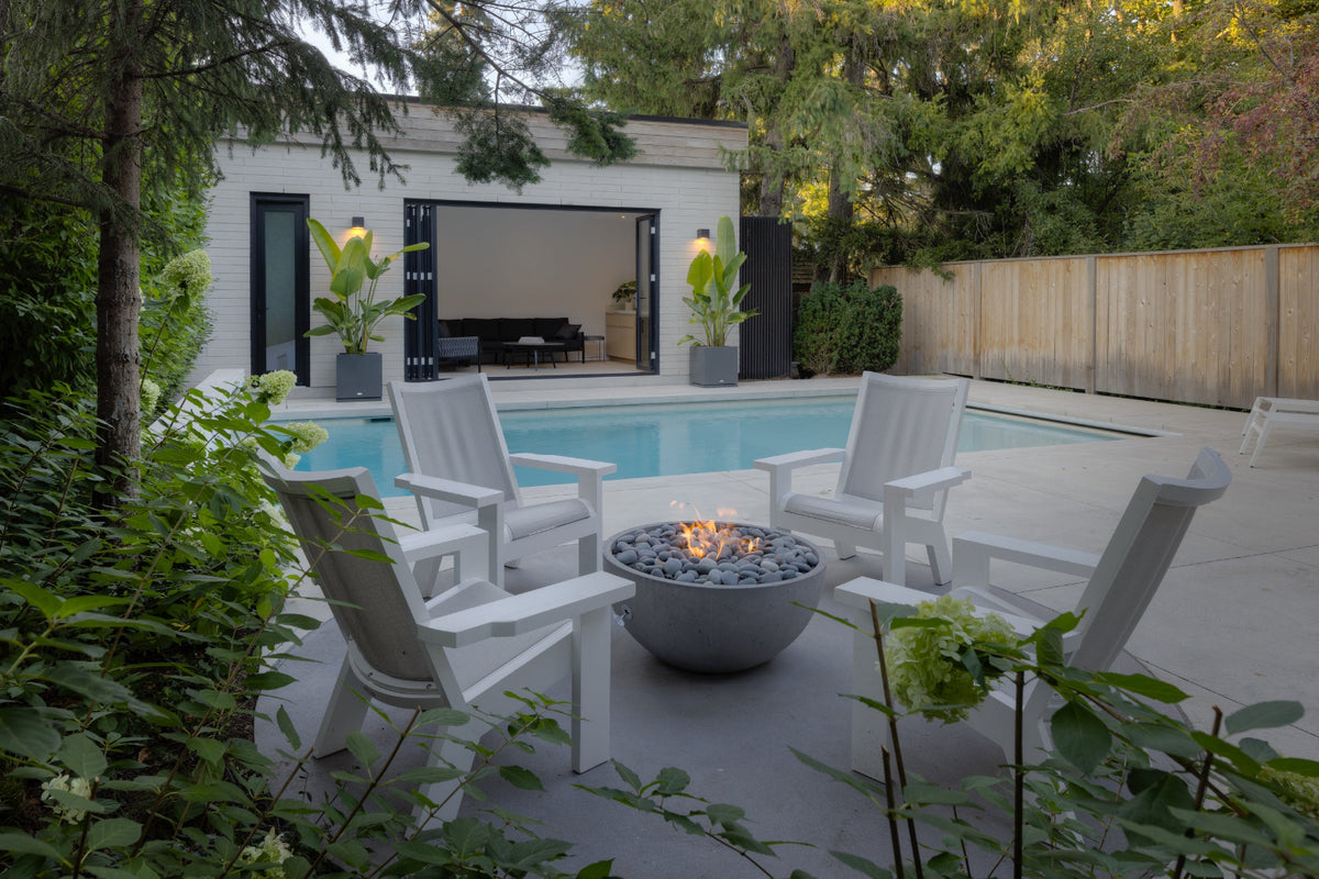 Outdoor patio with fire pit, chairs, and pool area surrounded by greenery