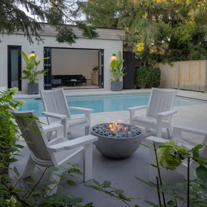 Outdoor patio with fire pit, chairs, and pool area surrounded by greenery
